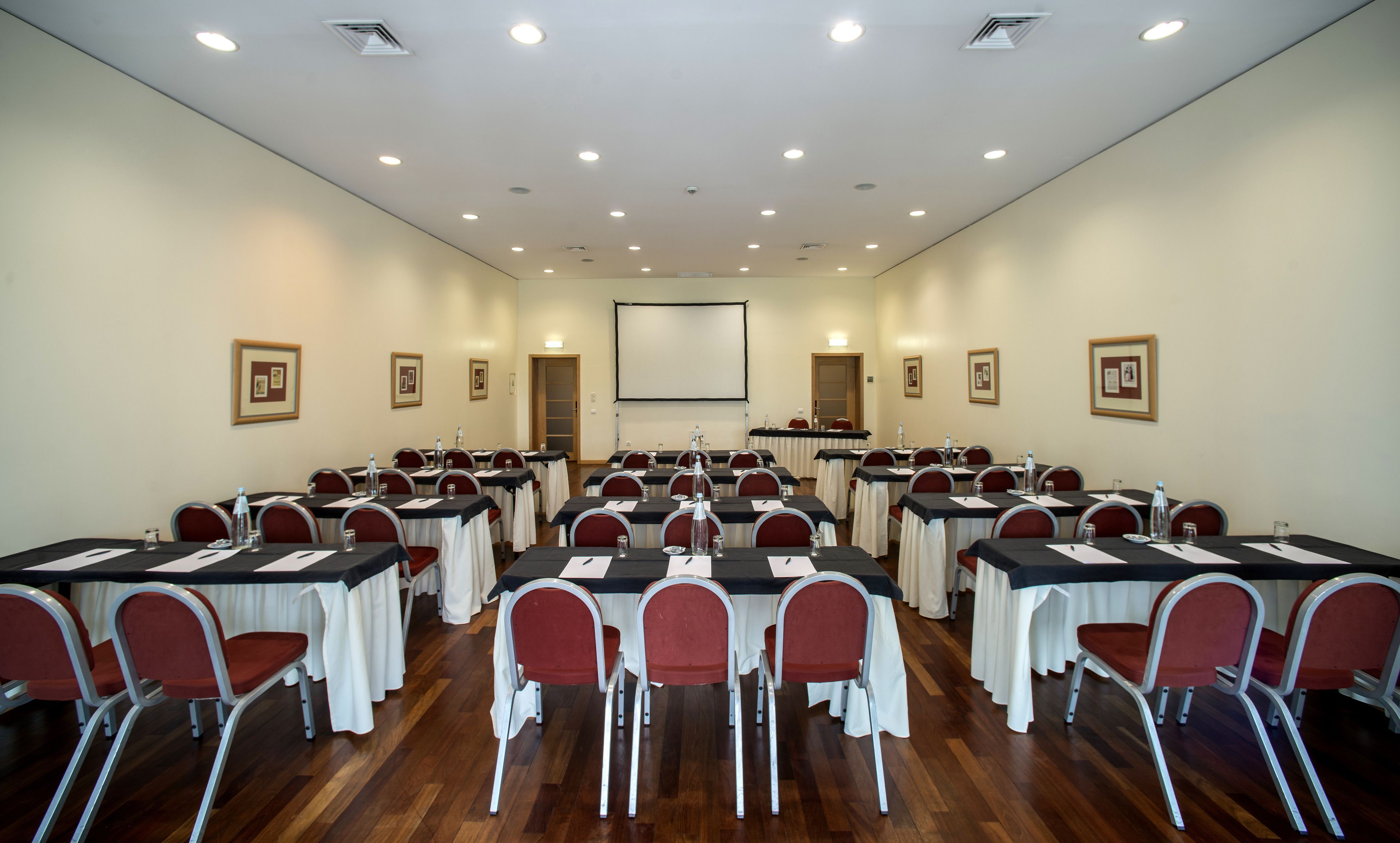 A conference room with tables and chairs, a projector screen, and framed pictures on the walls.