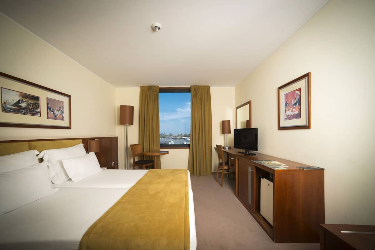 A hotel room with a bed, a desk, a television, and a window with curtains.
