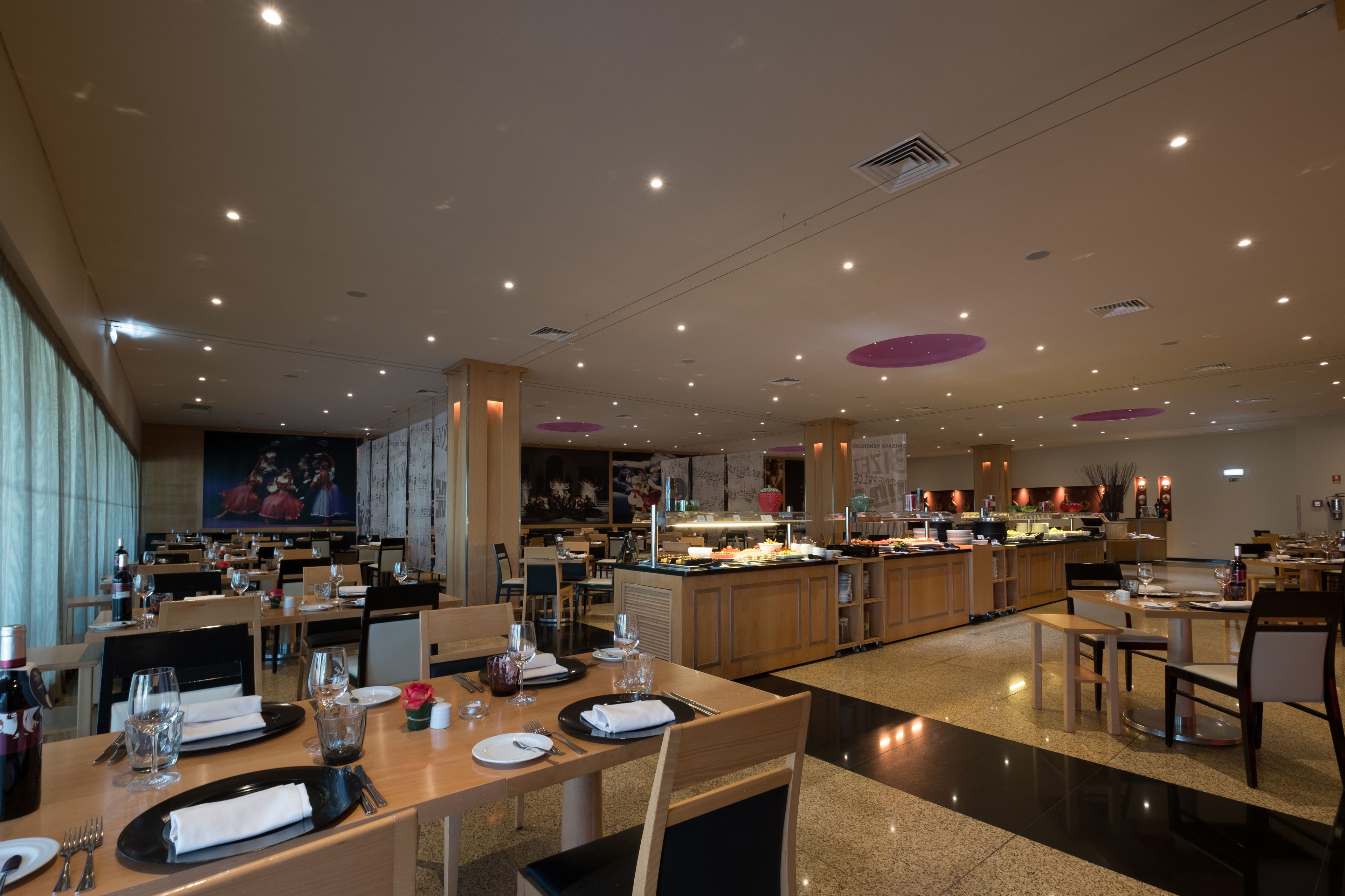 A spacious restaurant with multiple dining areas, a central bar, and a large mural on the wall.