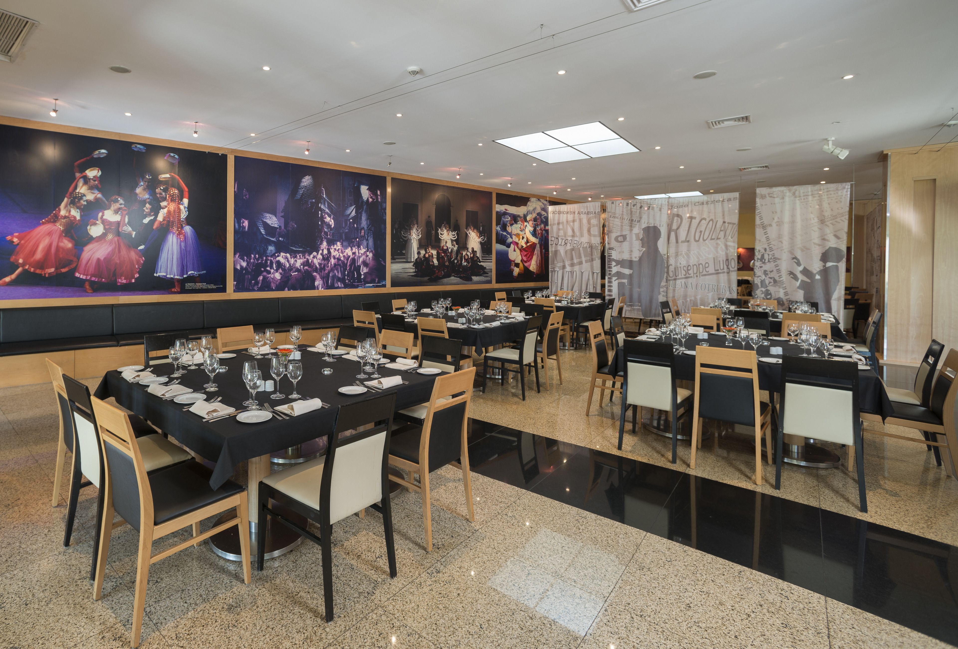 A restaurant with multiple tables set for dining, featuring a modern interior with a polished floor and large wall art depicting dancers.