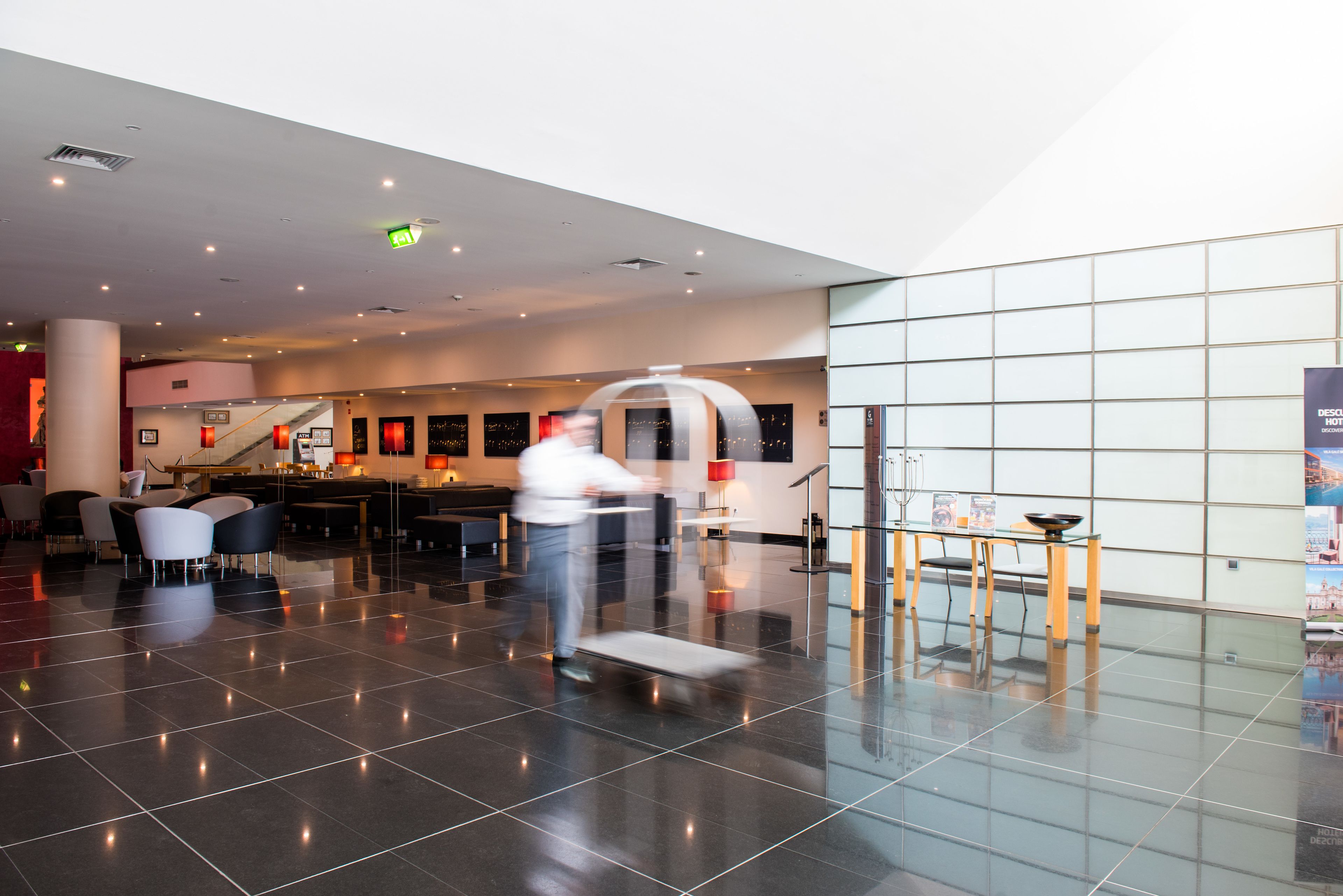 A spacious lobby with a modern design, featuring a central staircase, seating areas, and a glass partition wall.