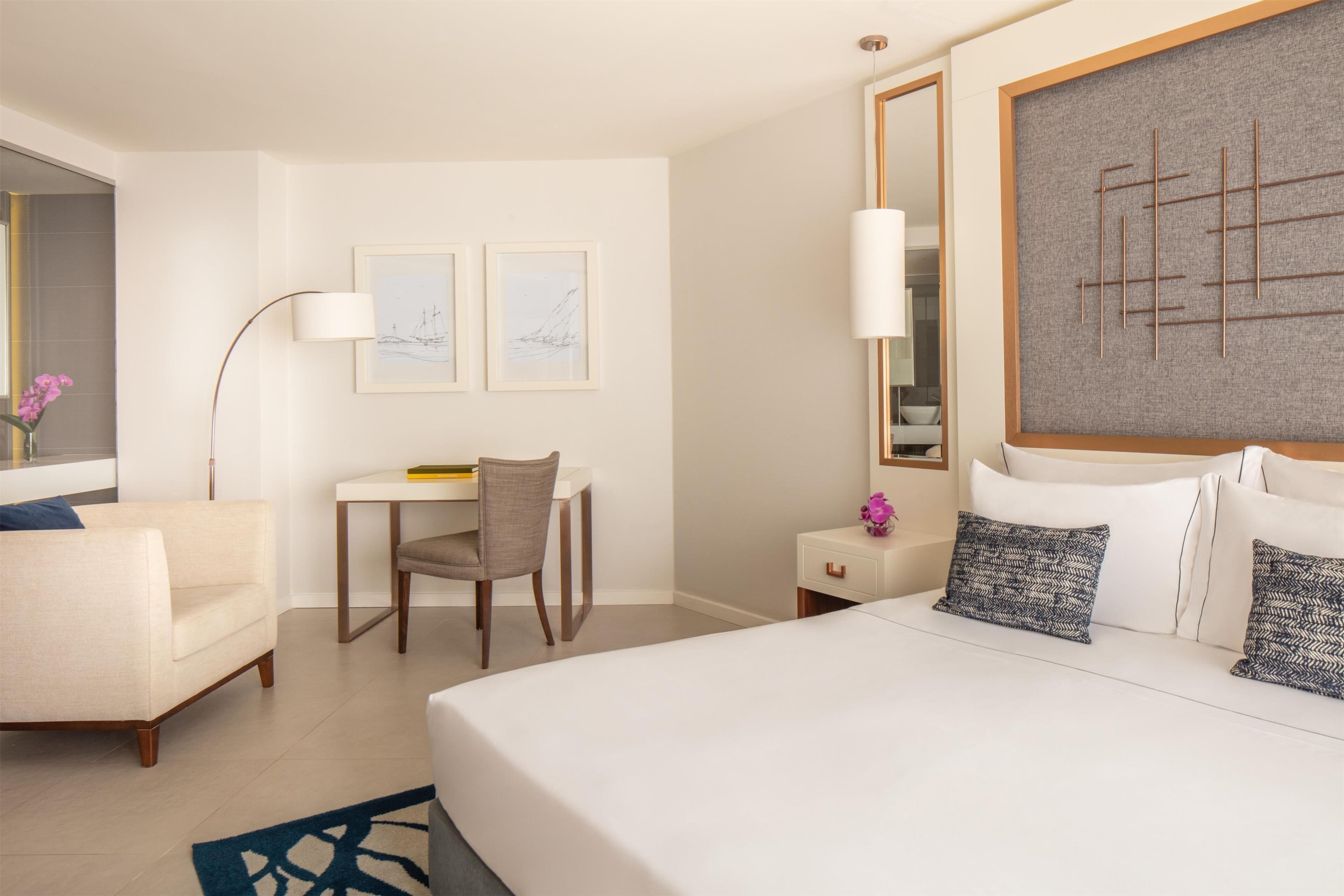 Une chambre d’hôtel avec un grand lit, un bureau, une chaise, une lampe et des œuvres d’art accrochées aux murs.