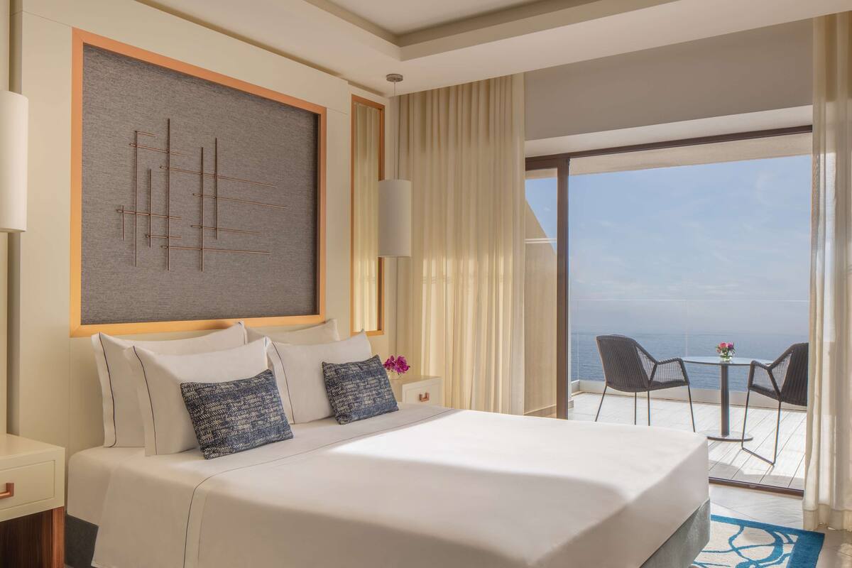 A hotel room with a large bed, a view of the sea, and a balcony with outdoor seating.