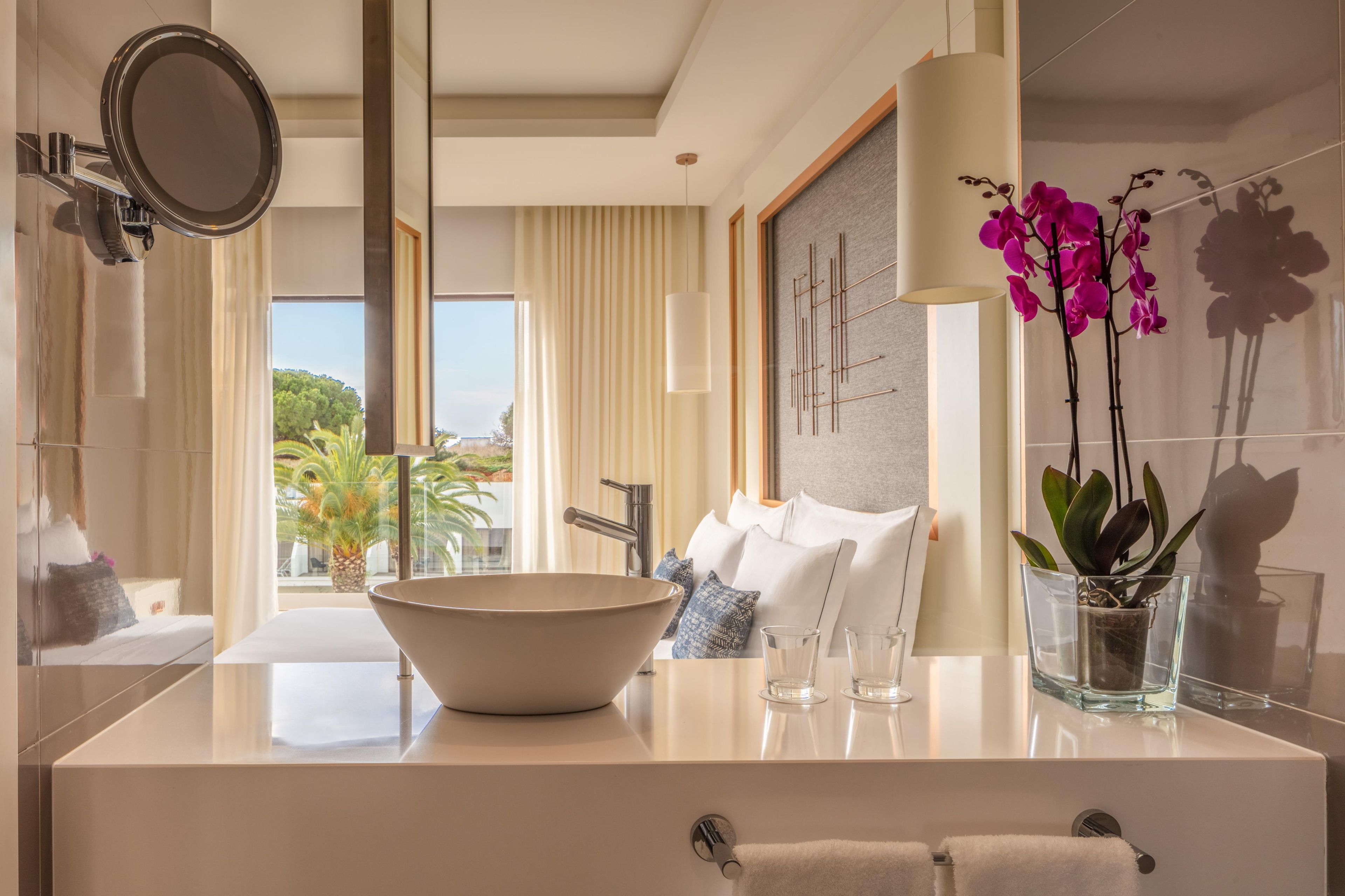 A modern bathroom with a large bowl sink, a mirror, a potted orchid, and a view of the outdoors.