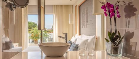 A modern bathroom with a large bowl sink, a mirror, a potted orchid, and a view of the outdoors.