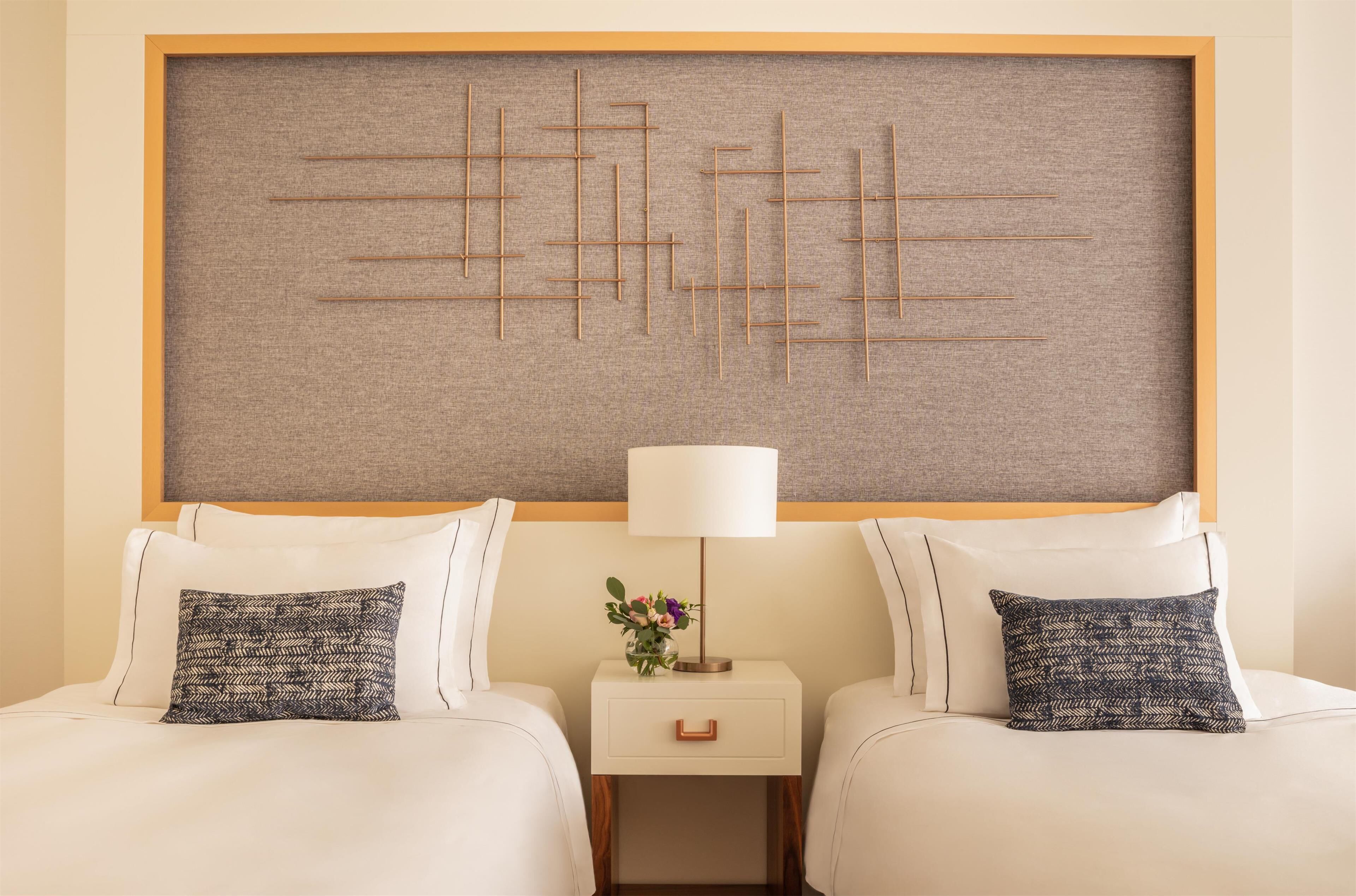 A hotel room with two beds, a nightstand with a lamp, and a decorative wall panel.