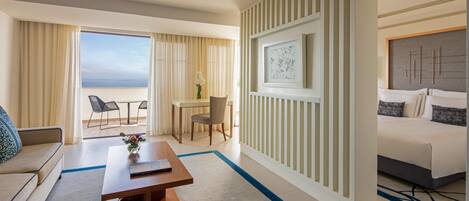 Habitación de hotel con cama, sofá, mesa de comedor y vistas al mar.