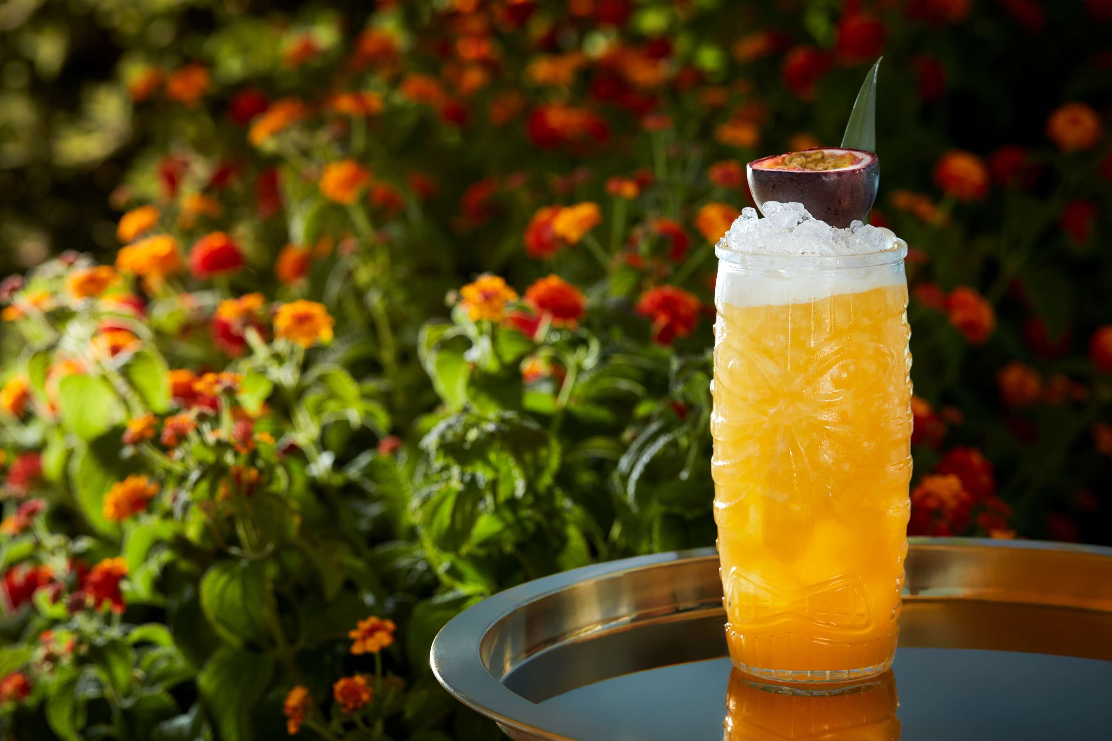 A glass of orange juice with ice and a slice of passion fruit on a metal tray.