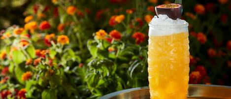 A glass of orange juice with ice and a slice of passion fruit on a metal tray.