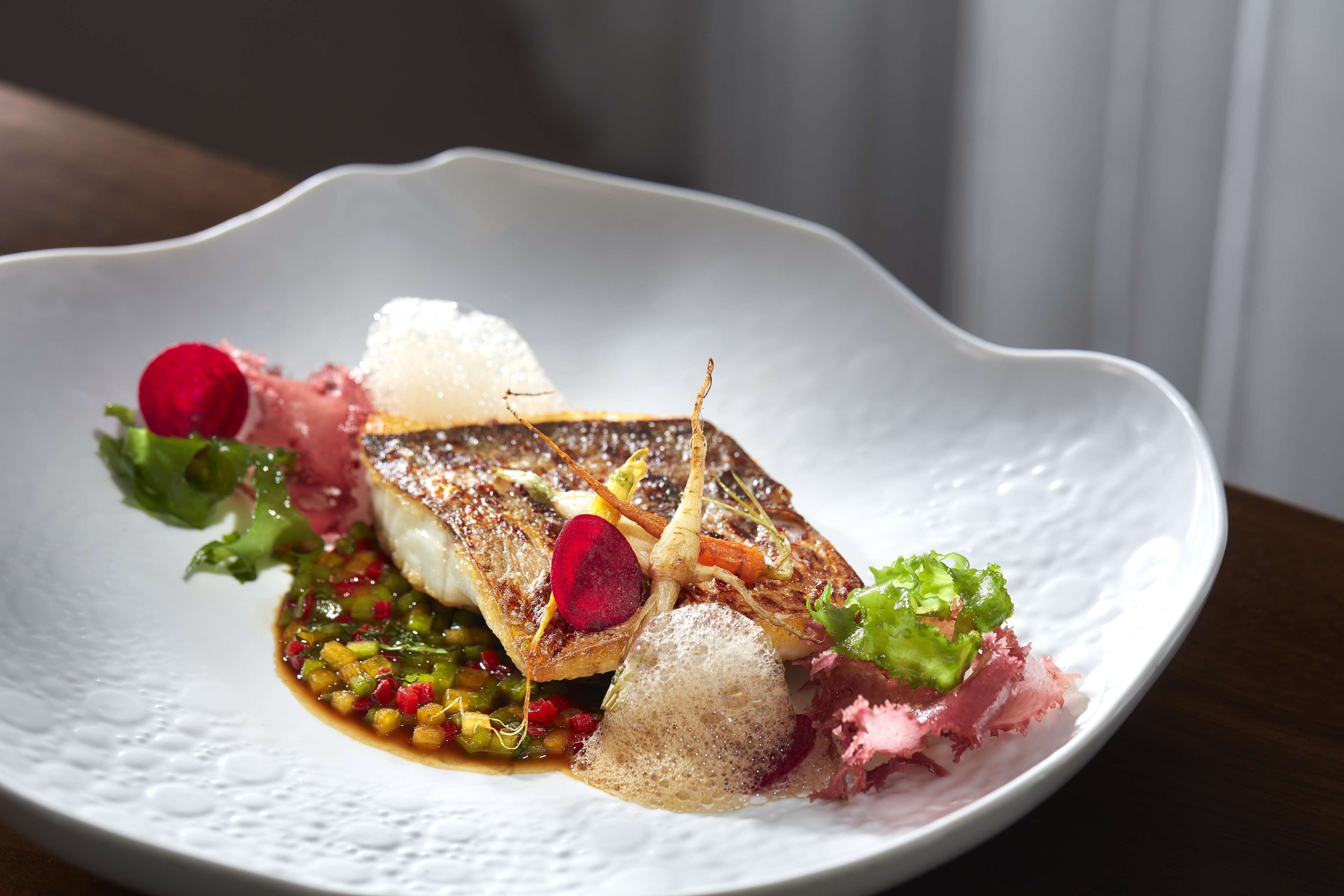 Une assiette blanche contenant un morceau de poisson, des légumes et une sauce.