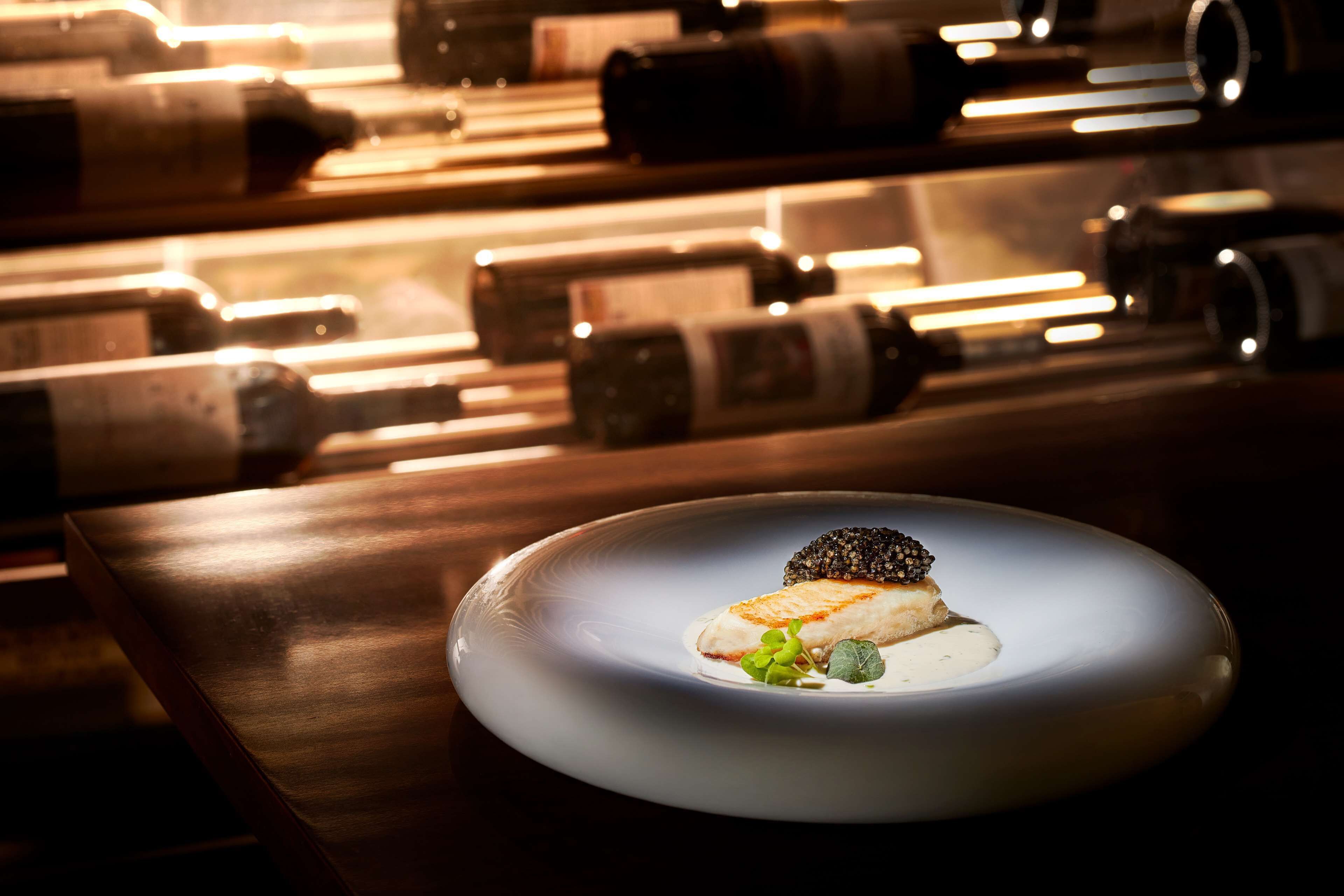 A dining table with a white plate of food, surrounded by wine bottles.