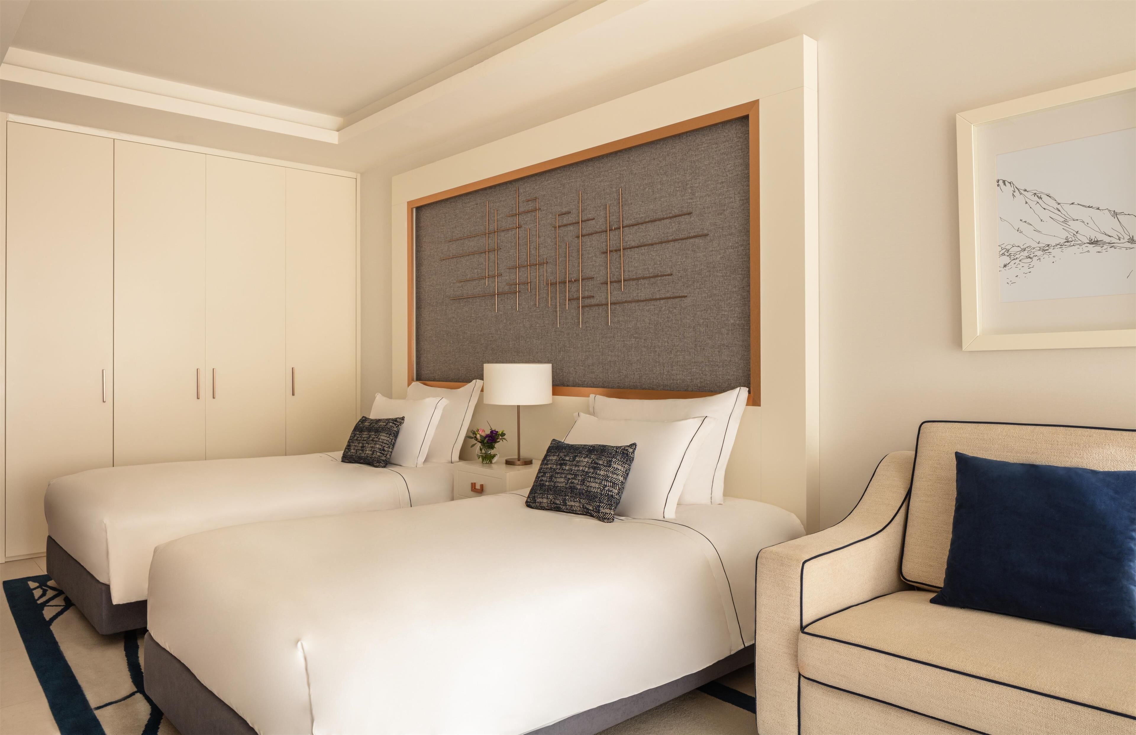 Habitación de hotel con dos camas, un sofá, una obra de arte grande en la pared y una fotografía enmarcada.