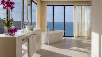 Un baño moderno con una bañera grande, un tocador con espejo y vistas al mar.