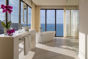 A modern bathroom with a large bathtub, a vanity with a mirror, and a view of the sea.