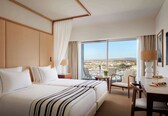 A hotel room with two beds, a dining area with a table and chairs, and a large window offering a city view.