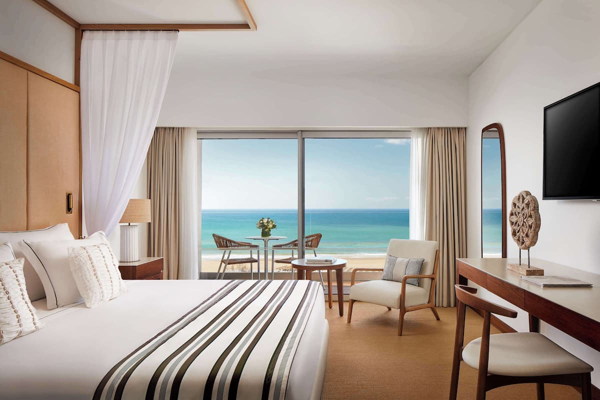 Een hotelkamer met een groot bed, een bureau, een stoel, een televisie en uitzicht op de oceaan.