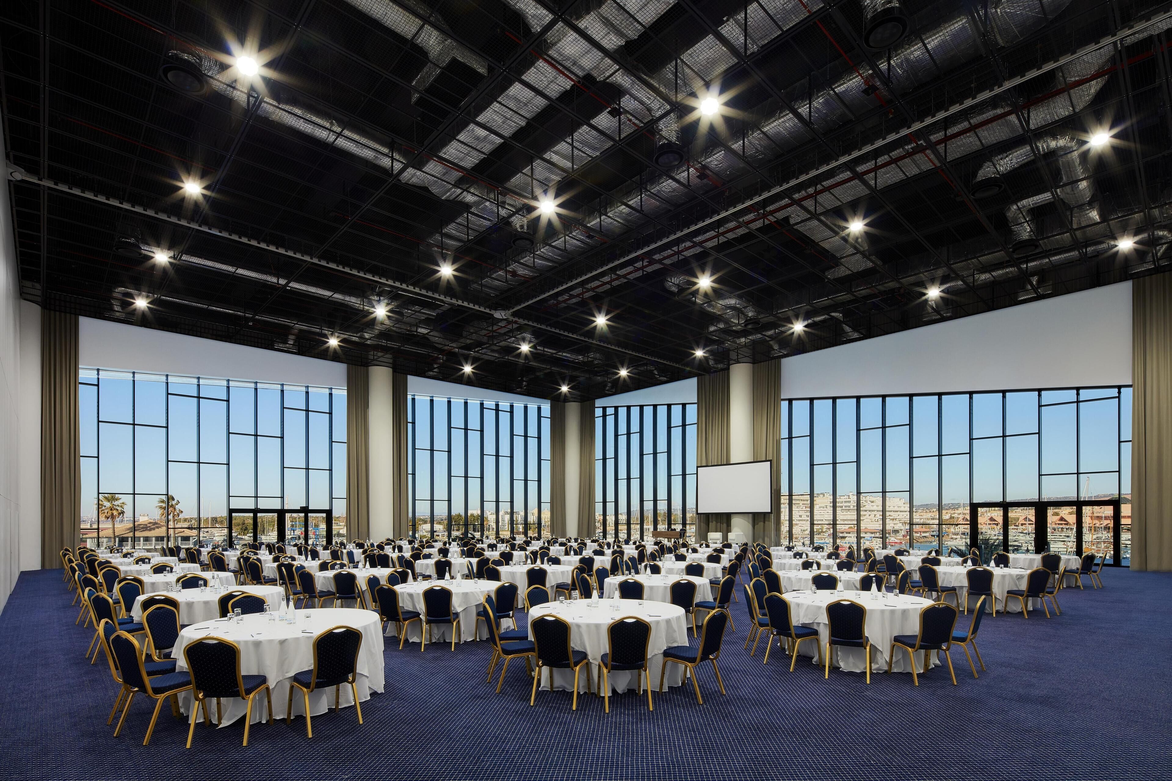A large conference room with round tables and chairs, large windows, and a city view.