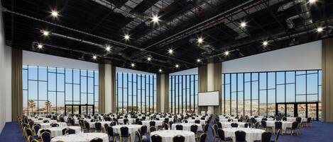 Un amplio salón de conferencias con mesas y sillas redondas, ventanas grandes y vistas a la ciudad.