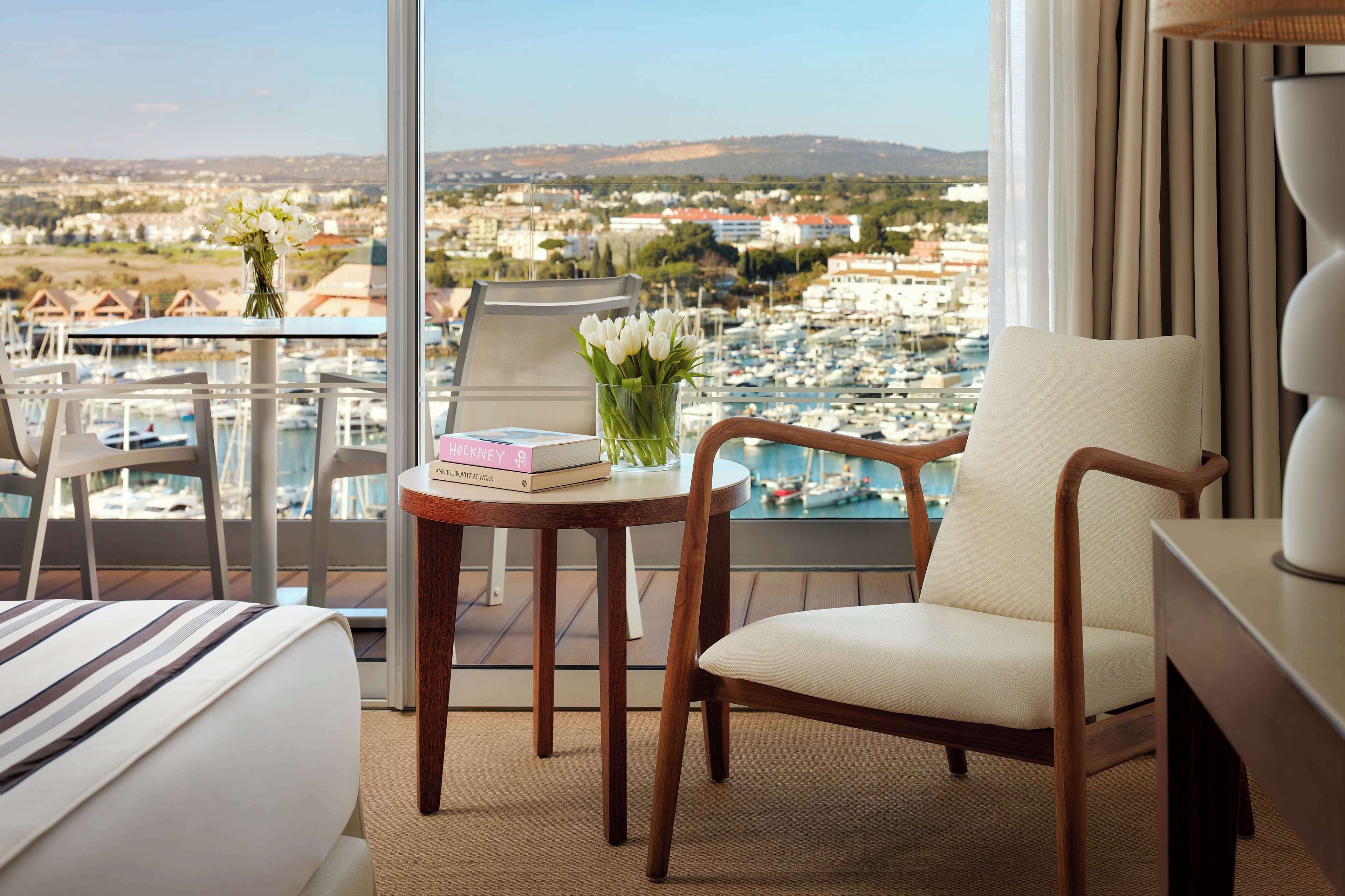 Une chambre d’hôtel avec un balcon donnant sur un port de plaisance et la ville.