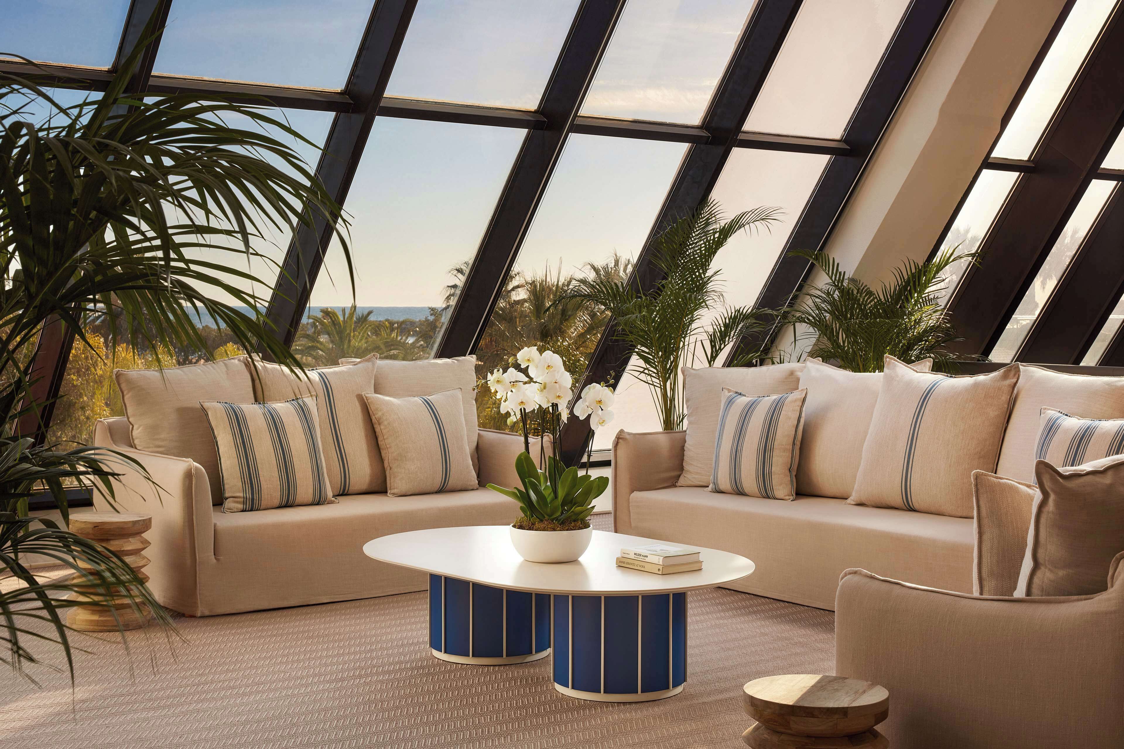 Un salón moderno con un sofá color beige, una mesa de centro redonda y vistas amplias a través de grandes ventanales.