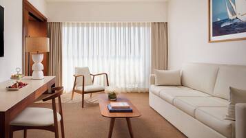 Ein modernes Hotelzimmer mit einem Holztisch, zwei Stühlen, einem Sofa und einem großen Fenster mit transparenten Vorhängen.