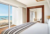 A hotel room with a large bed, a view of the beach, and a wooden floor.