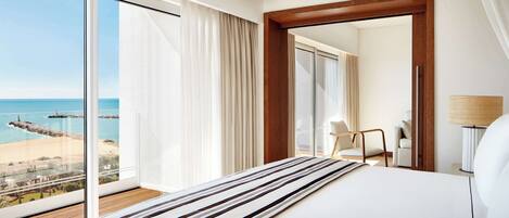 Habitación de hotel con una cama grande, vista a la playa y piso de madera.