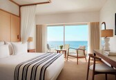 A hotel room with a large bed, a desk with a chair, a TV, and a view of the ocean.