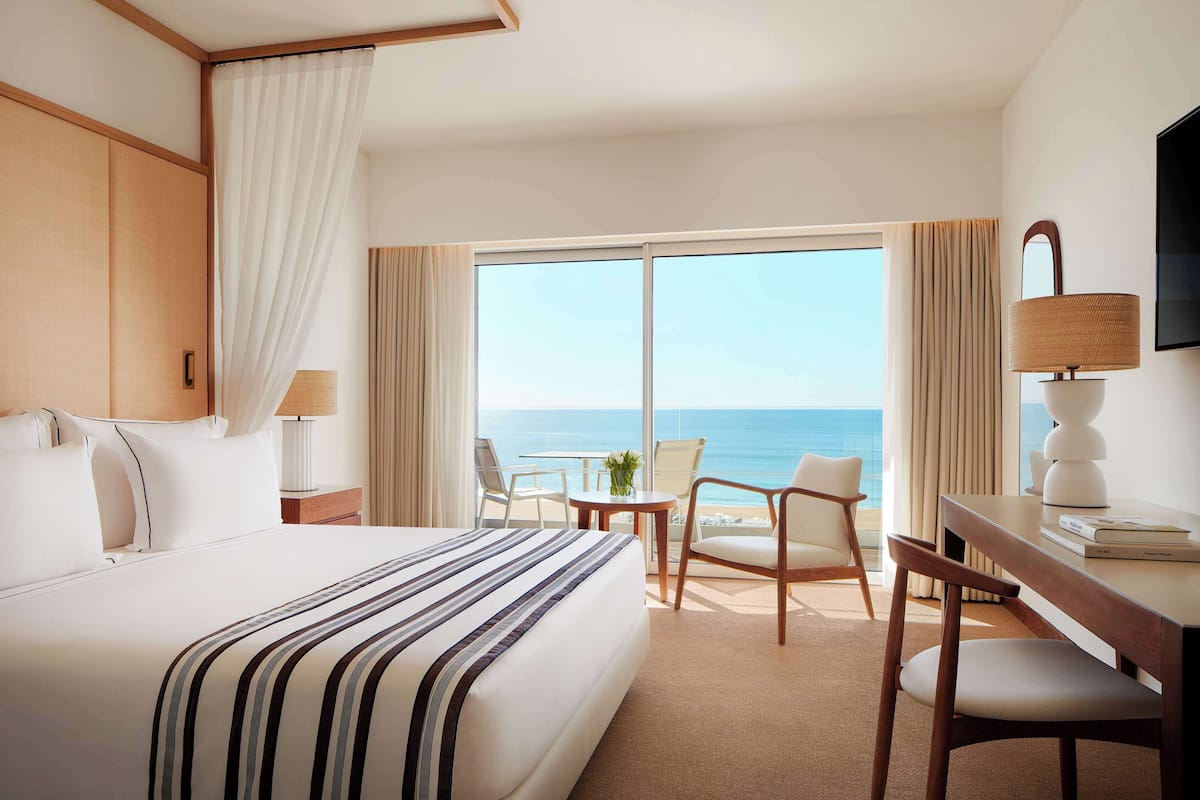 Een hotelkamer met een groot bed, een bureau met stoel, een televisie en uitzicht op zee.