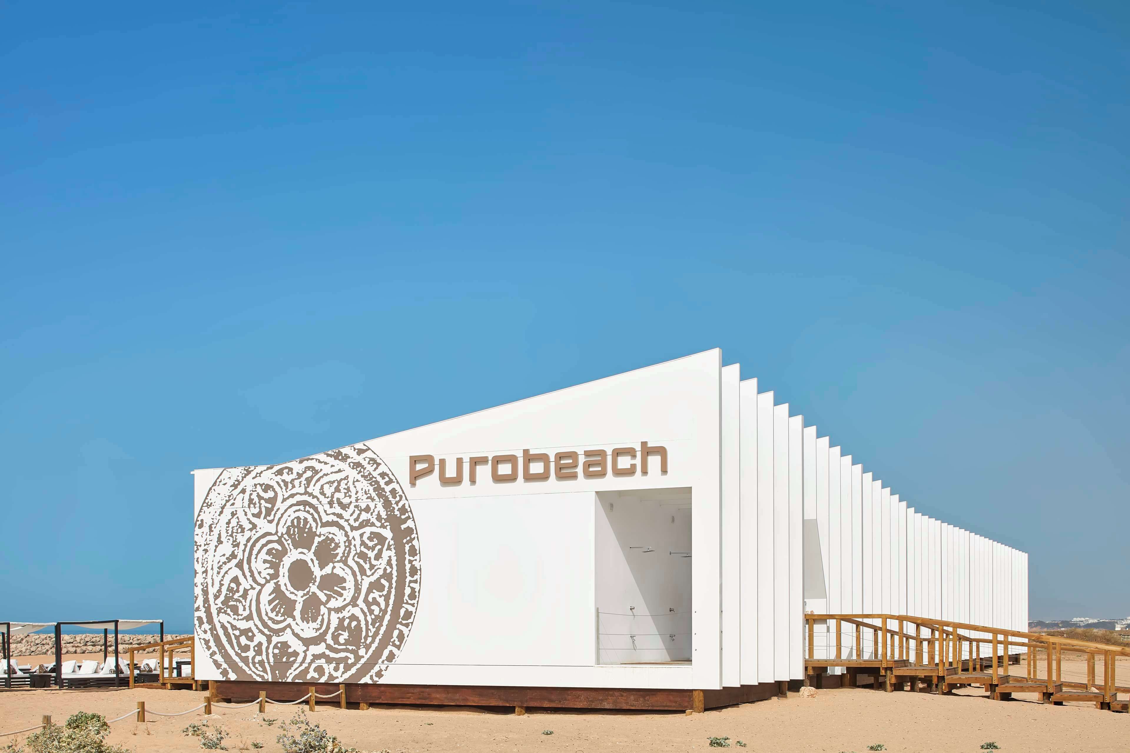A modern building with the name 'Purobeach' on its facade, featuring a large decorative panel and a wooden staircase leading to the entrance.