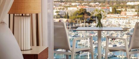 A balcony with a table and chairs, a vase of flowers, and a view of a marina and buildings.