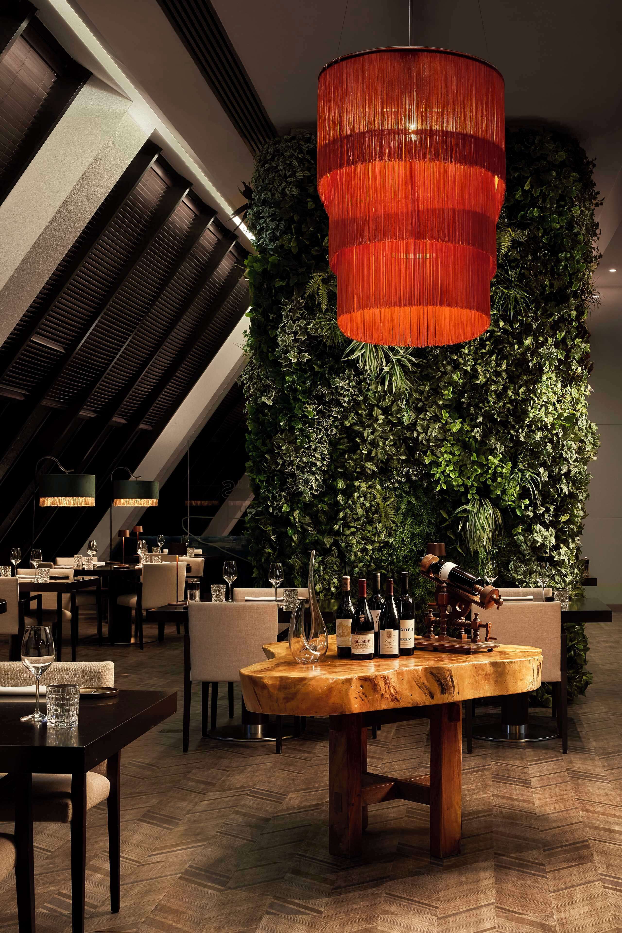 Un restaurant avec une table en bois, des bouteilles de vin et un luminaire rouge suspendu au plafond.