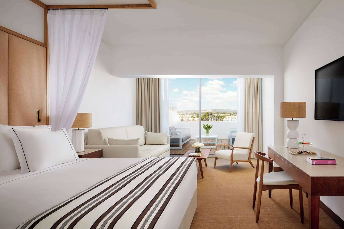 Hotelkamer met een bed, een slaapbank, een bureau, een stoel, een televisie en uitzicht op de stad.