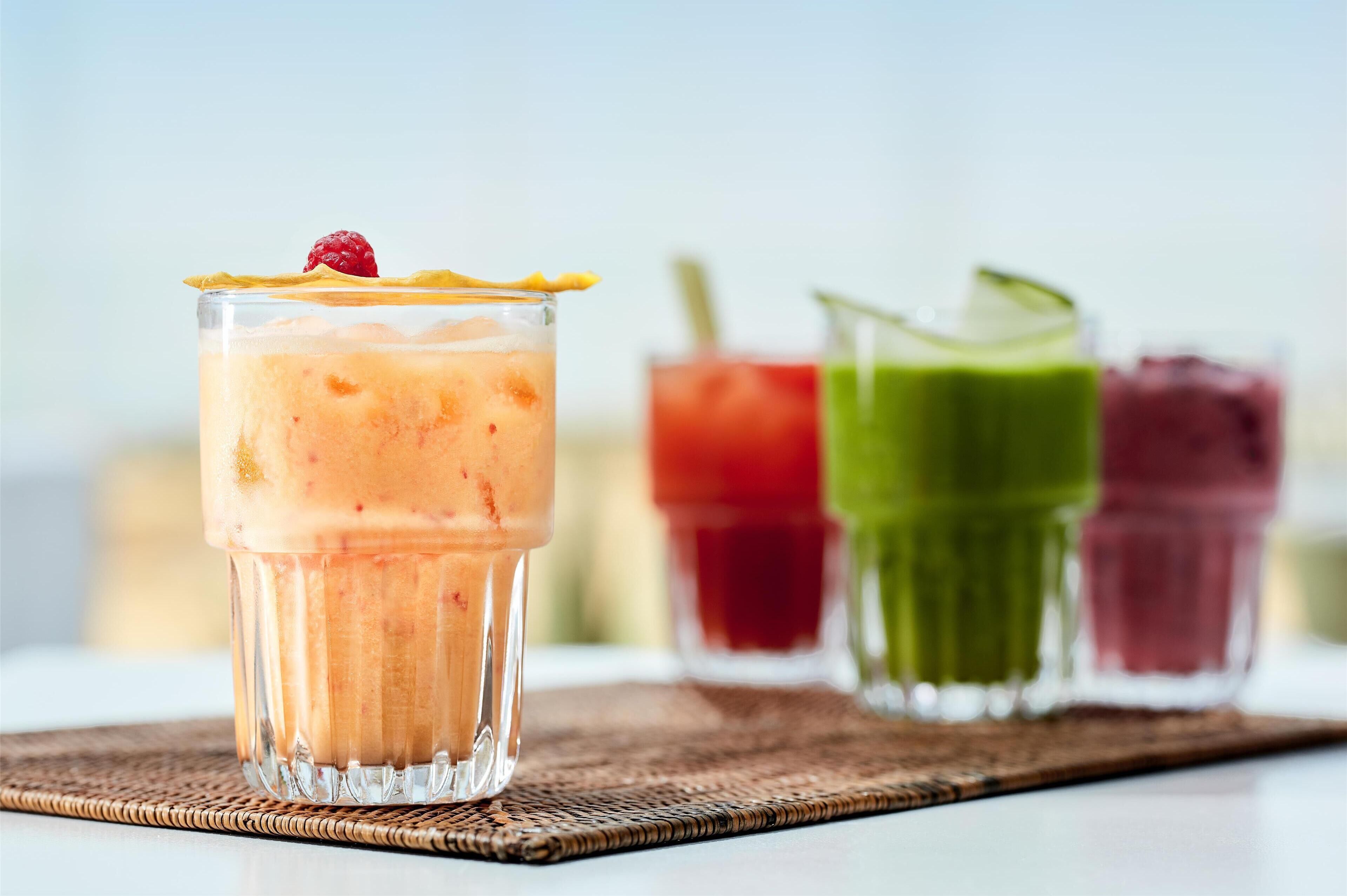 Un verre de smoothie, surmonté d’une framboise, posé sur un tapis tressé.
