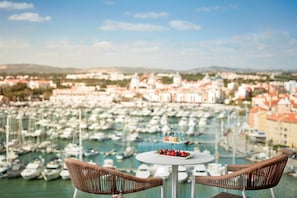 A balcony with wicker chairs and a small table with fruit, overlooking a marina with numerous boats.