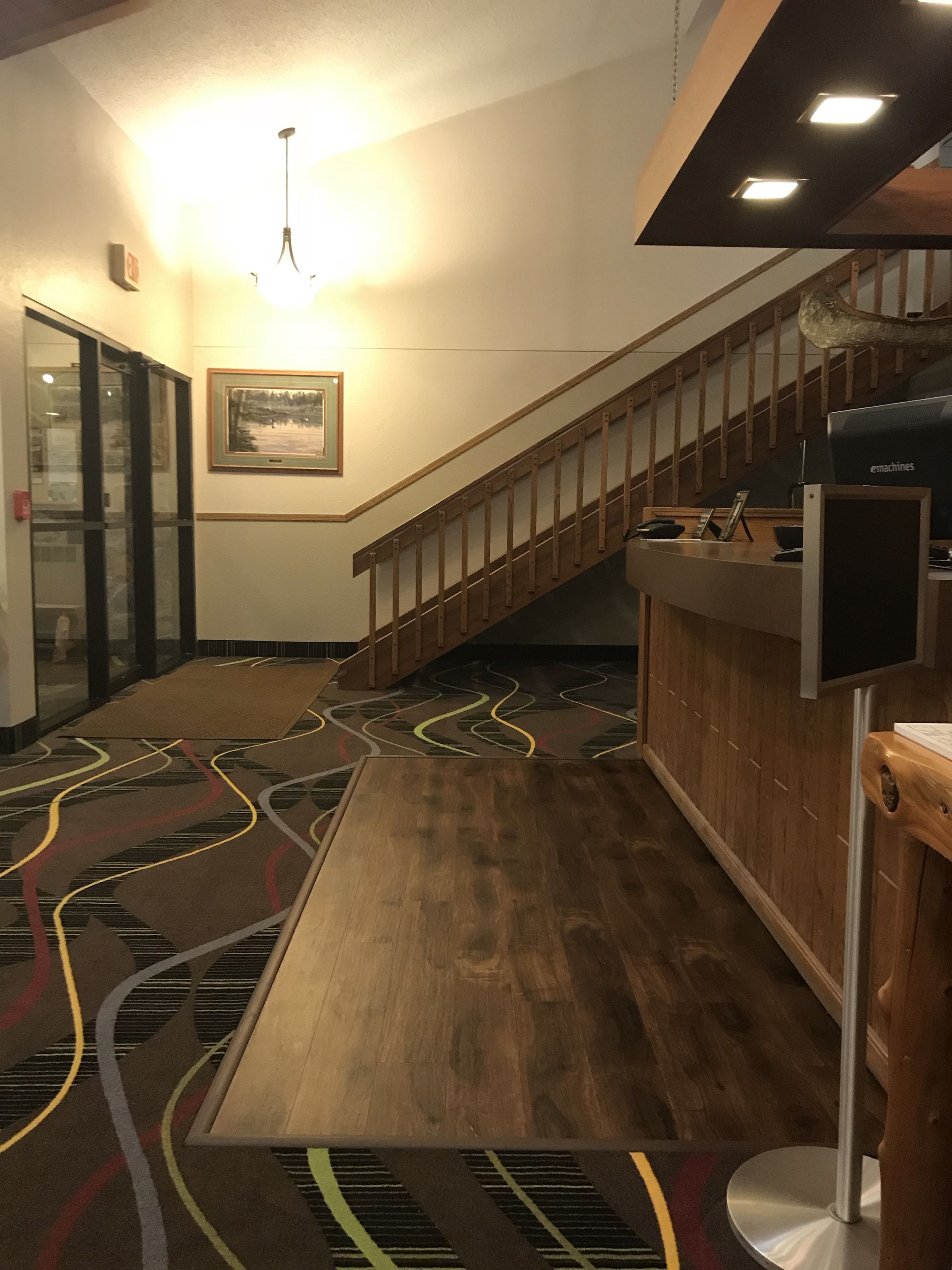 Un hall d’hôtel avec un escalier en bois, un comptoir d’accueil et une moquette à motifs.