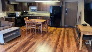 A modern kitchen with dark cabinets, a black refrigerator, and a dining area with wooden chairs and a table. - Walker Hotel (Walker)