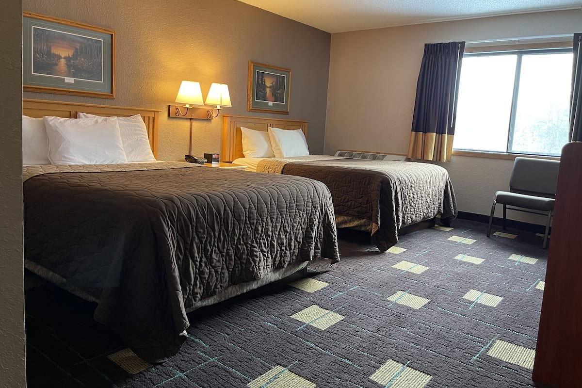 Ein Hotelzimmer mit zwei Betten, einem Schreibtisch, einem Stuhl und einem Fenster mit Vorhängen.