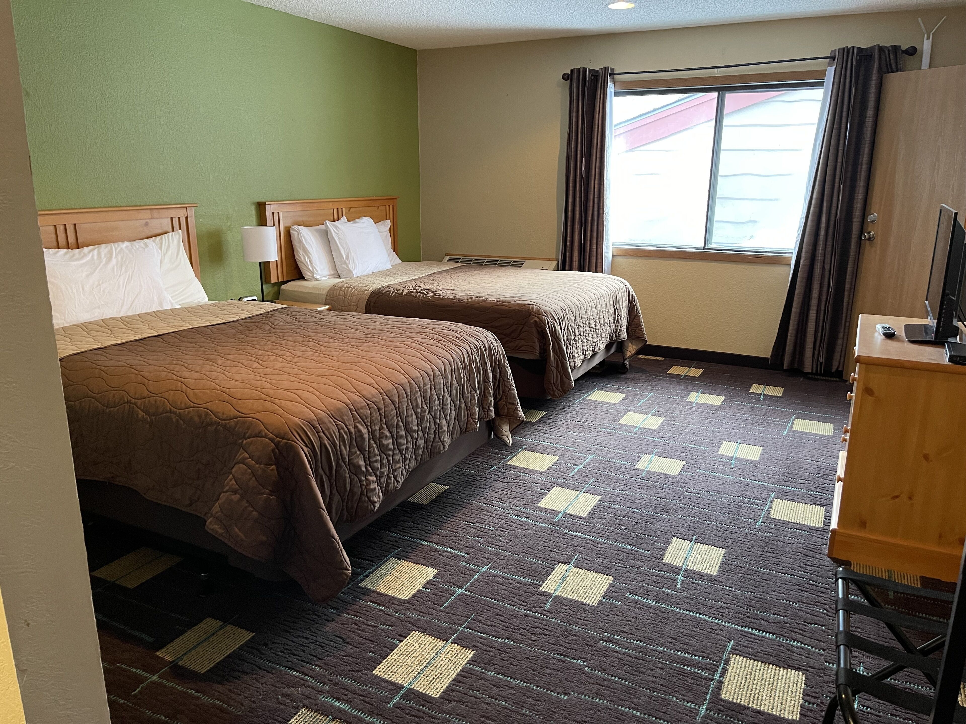 A hotel room with two beds, a television, and a window with curtains.