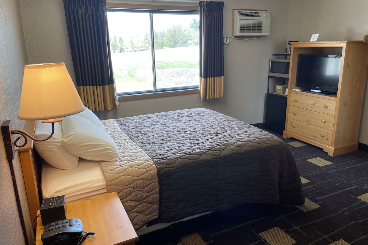 Ein Hotelzimmer mit einem Bett, einem Schreibtisch mit Lampe, einem Telefon, einem Schminktisch und einem Fernseher sowie einer Klimaanlage.