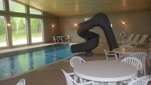 An indoor swimming pool with a slide, white plastic chairs, and tables arranged around the pool area. - Walker Hotel (Walker)