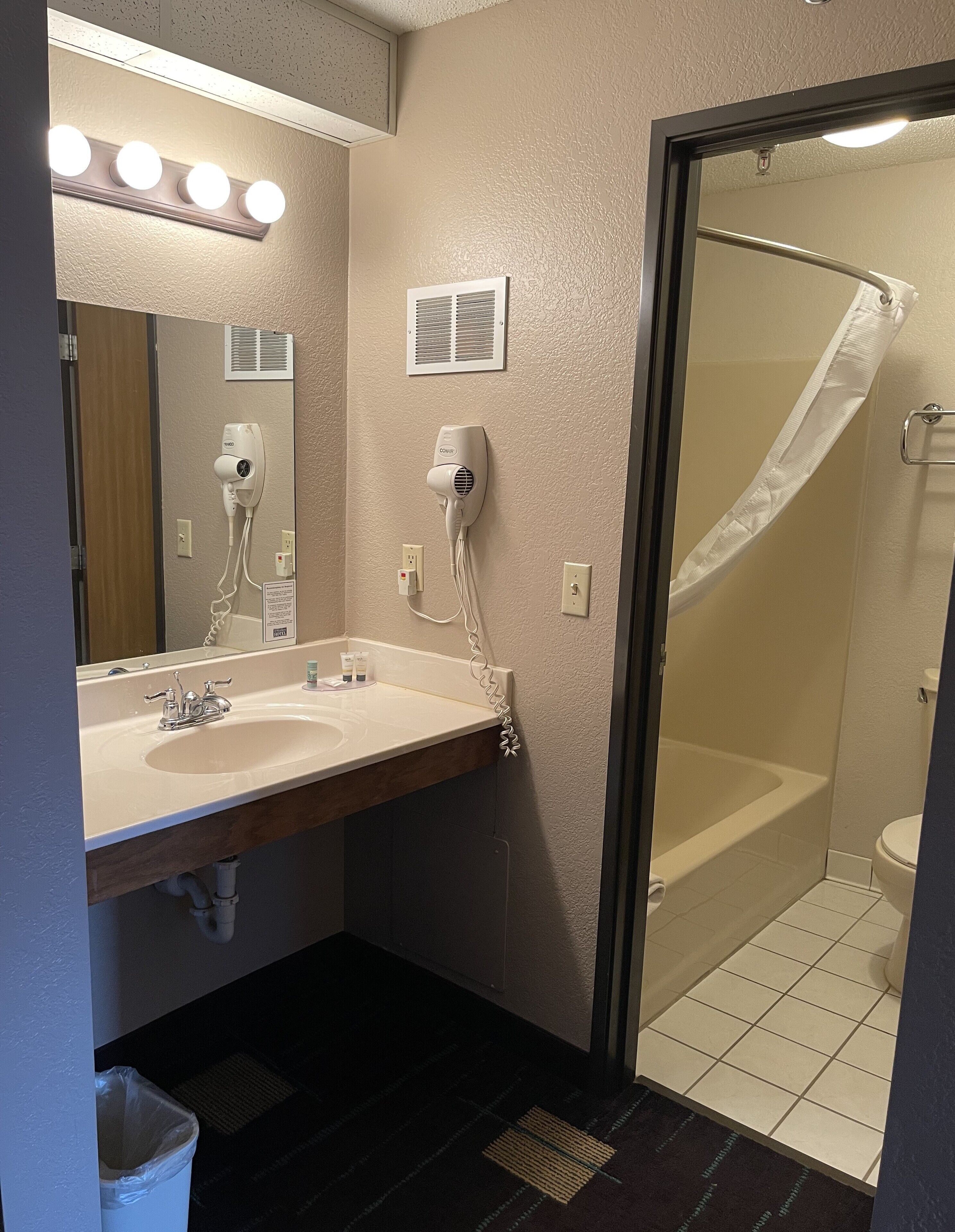 A bathroom with a sink, mirror, hairdryer, and shower with a curtain.
