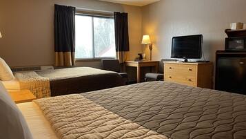 A hotel room with two beds, a desk with a lamp, a television, and a refrigerator.
