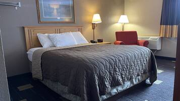 A hotel room with a bed, two bedside lamps, a red chair, a framed picture on the wall, and a thermostat on the wall.