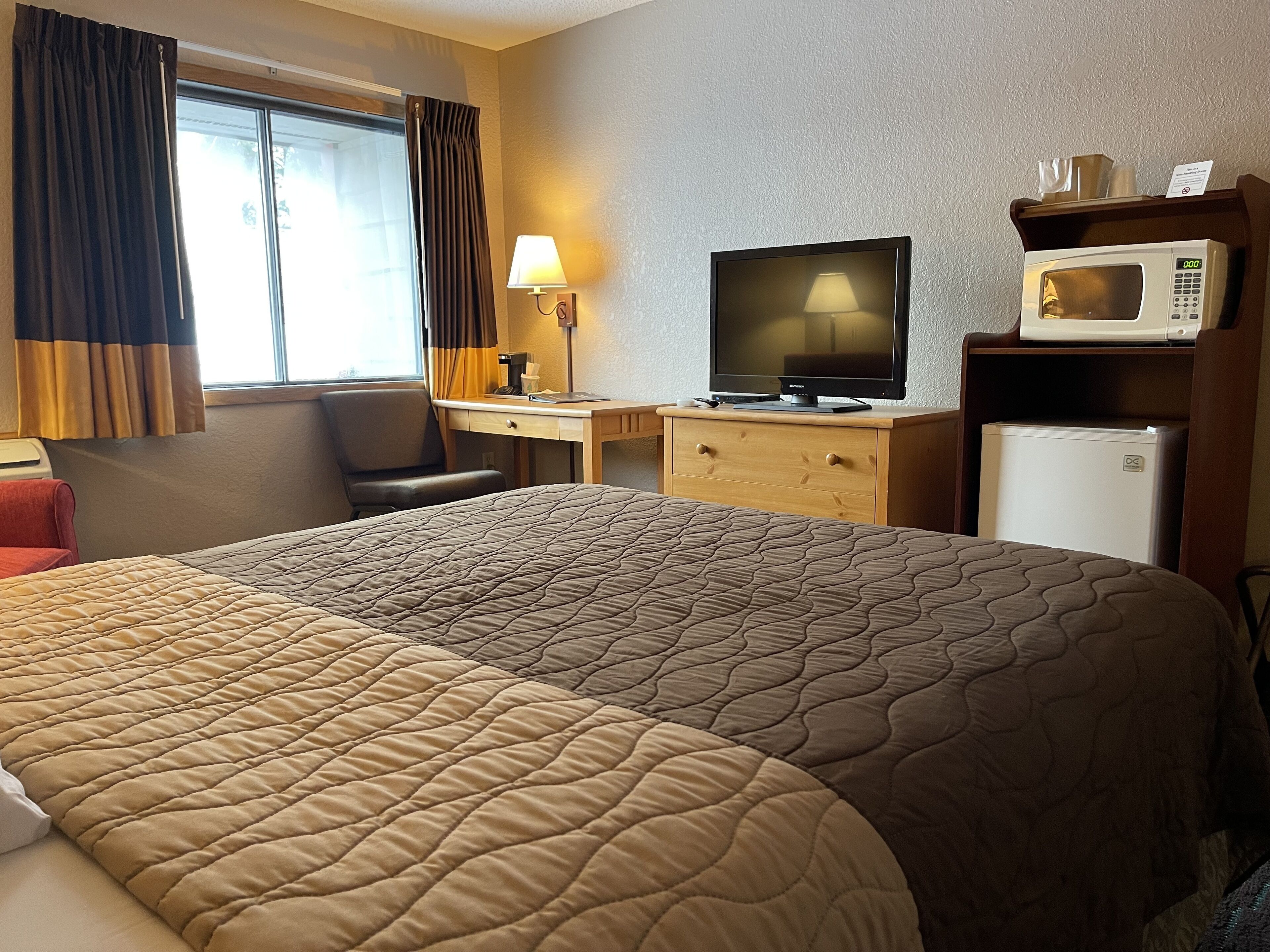 A hotel room with a large bed, a desk with a television, a microwave, and a refrigerator.