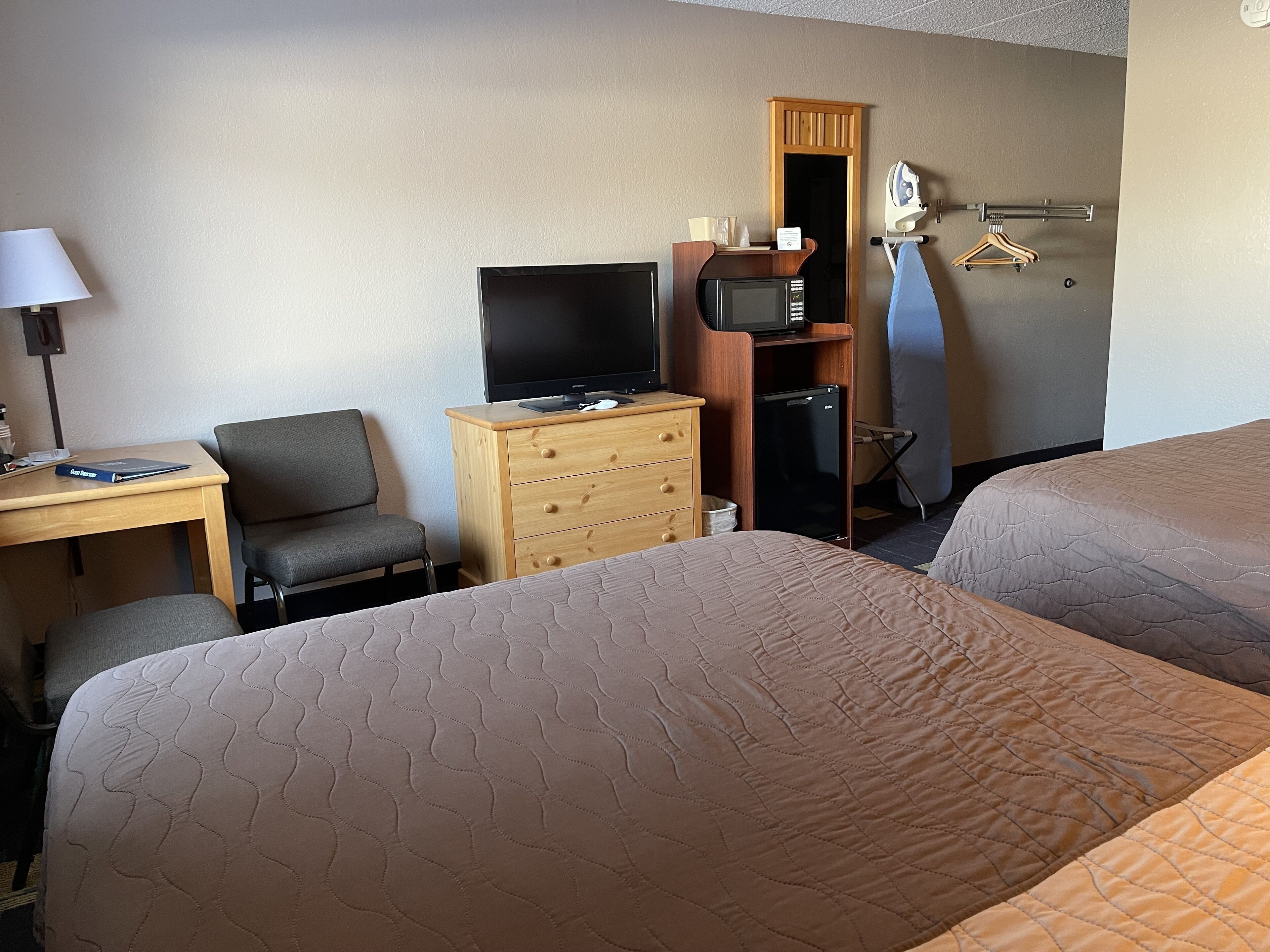 A hotel room with two beds, a desk with a computer, a TV, a dresser, and a microwave.