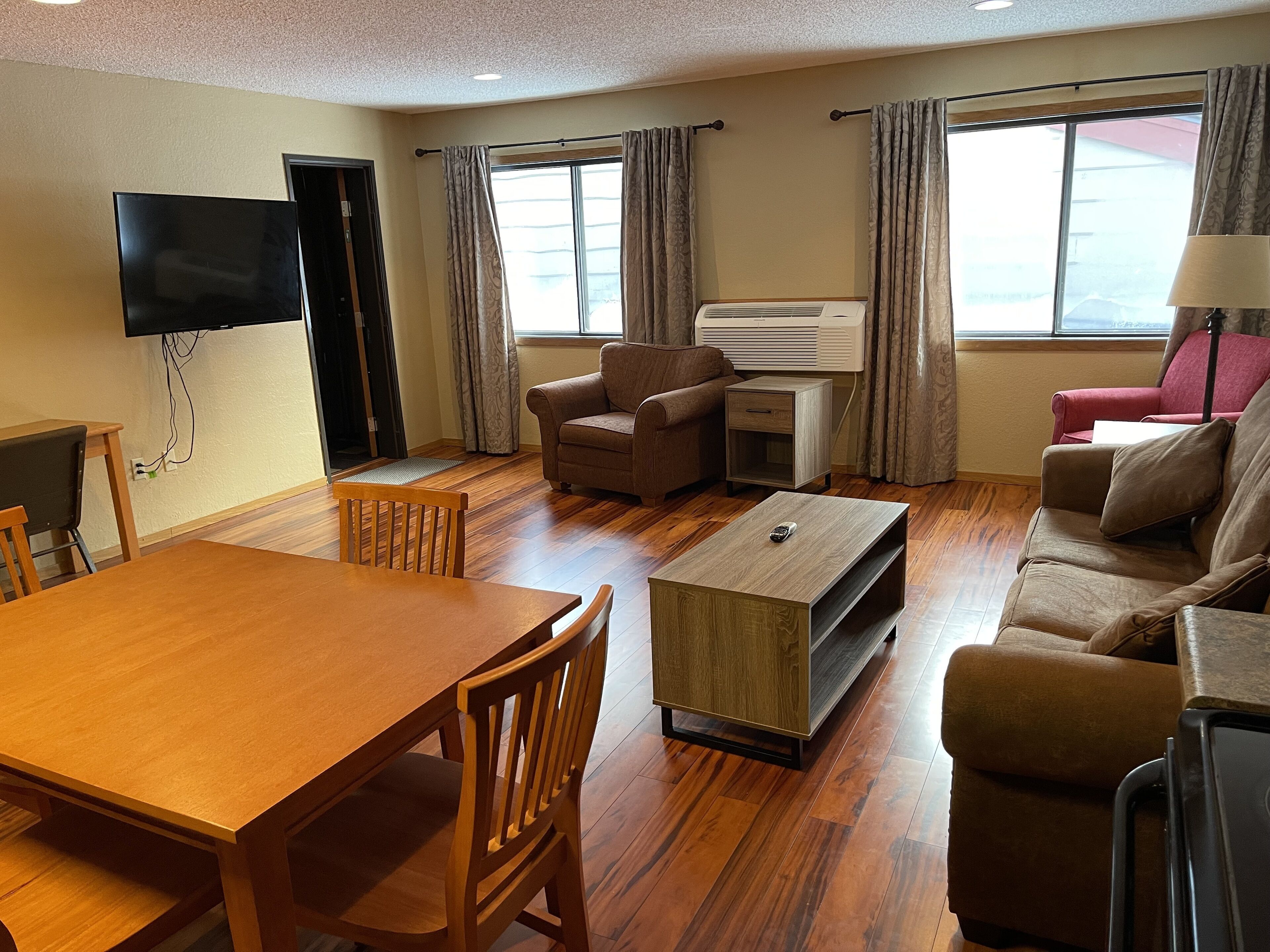 A furnished living room with a wooden dining table, two sofas, a coffee table, and a TV mounted on the wall.