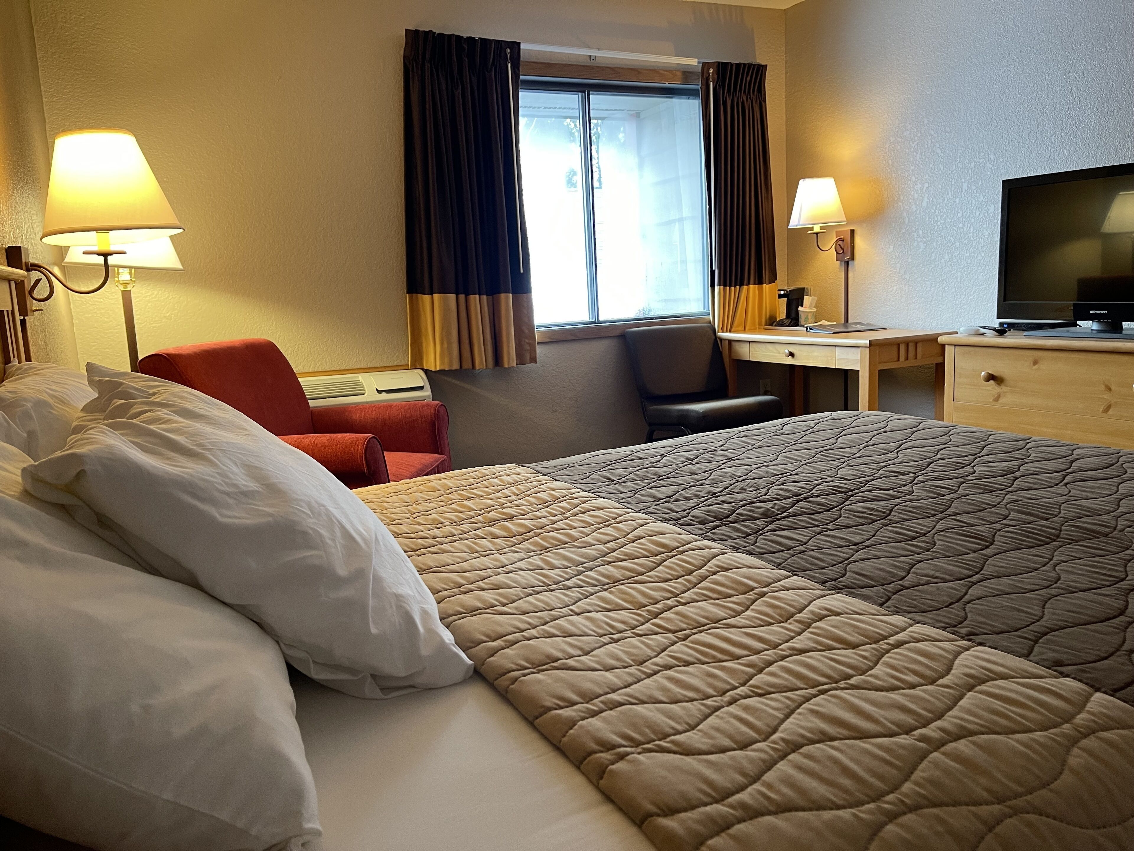 Une chambre d’hôtel avec un grand lit, deux lampes de chevet, un bureau avec une chaise, une télévision et une fenêtre avec des rideaux.