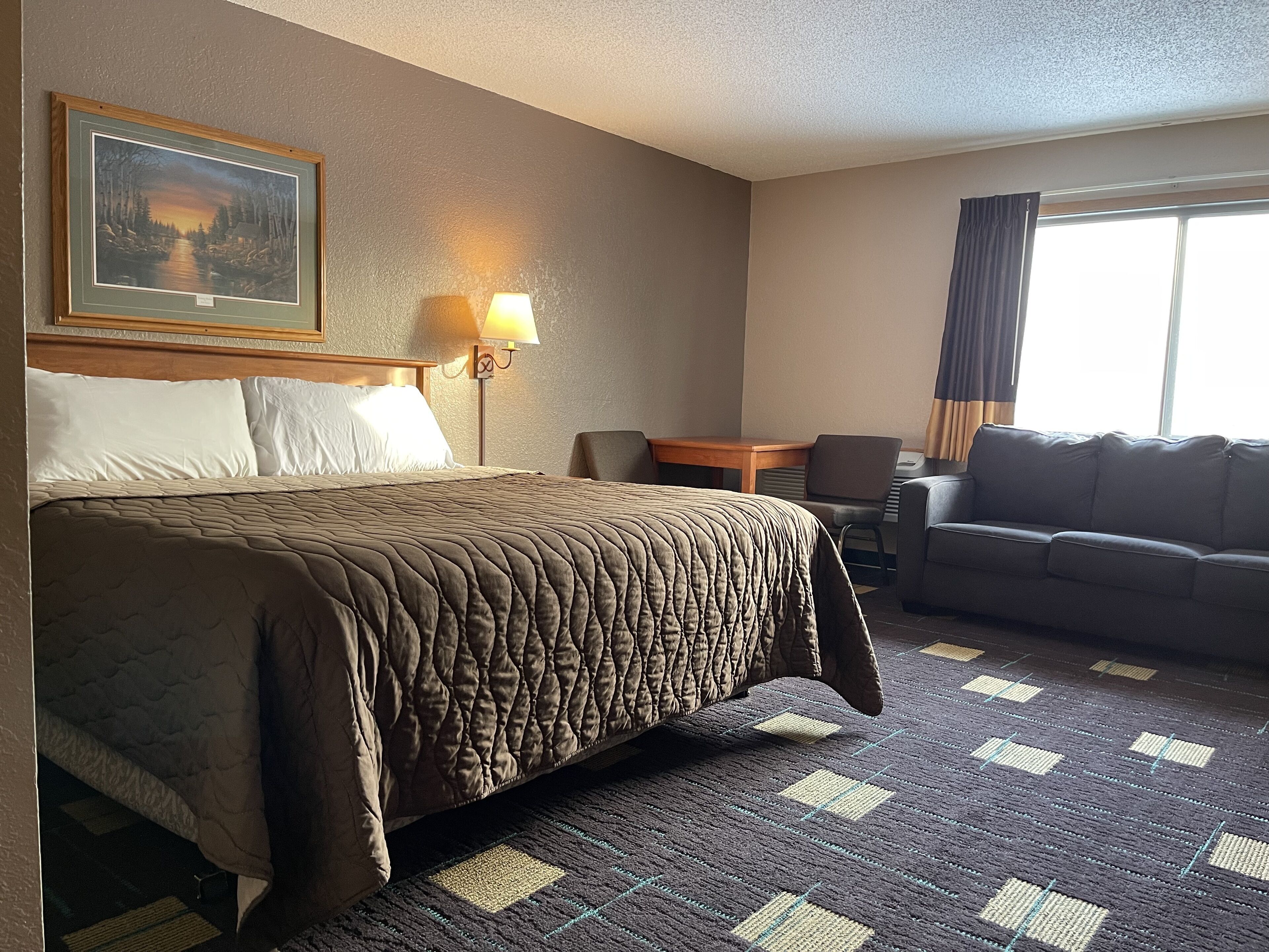 Habitación de hotel con una cama grande, un sofá, una mesita, una lámpara y un cuadro en la pared.