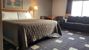 A hotel room with a large bed, a sofa, a small table, a lamp, and a painting on the wall.